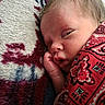 baby, blanket, cheek, child, close_up, cozy, face, fist, head, indoors, infant, newborn, patterned, peaceful, portrait, red, resting, sleeping, swaddled, textile