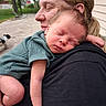 Kaden is registered to the contest to win money with this photo: baby, newborn, sleeping, adult, woman, outdoor, backyard, dog, green_clothing, hug, shoulder, person, rest, face, head, skin, hair, fence, tree, smile