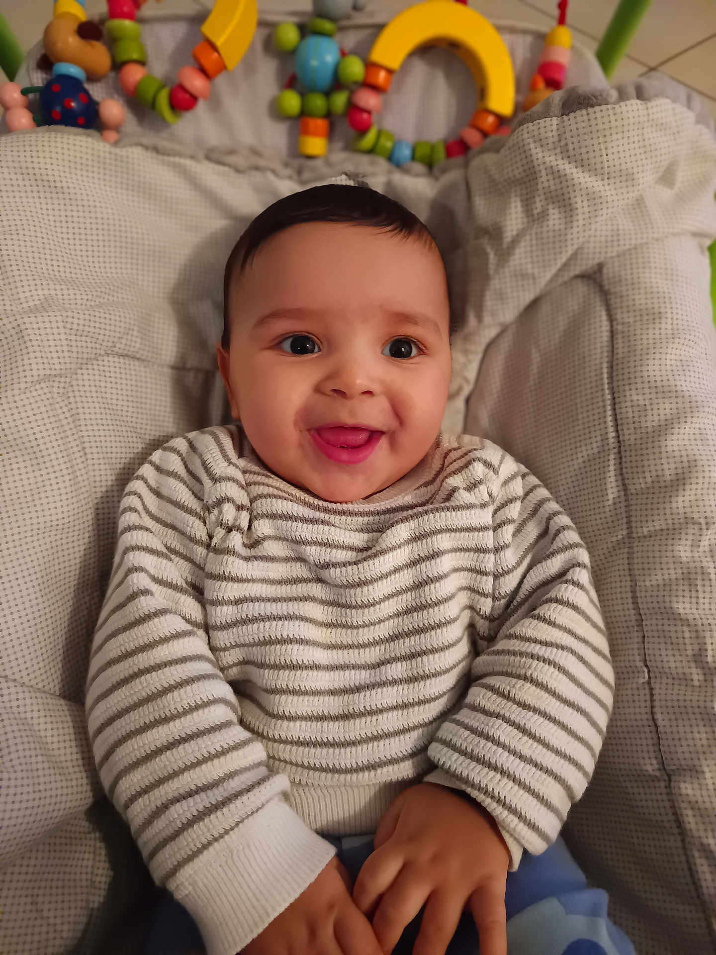 Naël participe au concours pour gagner de l'argent avec cette photo : baby, smiling, infant, striped_sweater, baby_seat, toys, colorful, happy, child, cute, indoor, cozy, hands, face, portrait, comfort, soft, cushion, play, young