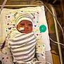 newborn, baby, hospital, crib, swaddle, striped_clothing, hat, bear_ears, medical_tubes, monitoring_equipment, pillow, heart_pattern, infant, lying_down, face, cute, patient, healthcare, wrapped, small
