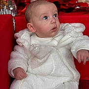 Lyam a rejoint le concours — aidez-le/la à gagner de superbes lots ! baby, infant, blue_eyes, white_outfit, fur_suit, zipper, red_background, gift_wrap, bow, couch, sofa, portrait, close_up, cute, looking_up, expression, holiday, soft_texture, small_hands, seat