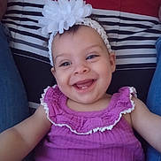 Nevaeh is registered to the contest to win money with this photo: baby, child, smile, headband, flower, purple_dress, happy, face, person, cushion, striped_background, legs, seated, indoors, cute, infant, joy, apparel, portrait, closeup