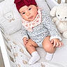Ailany is registered to the contest to win money with this photo: baby, infant, child, crib, nursery, sleeping_area, bunny, stuffed_animal, teddy_bear, bow_hat, floral_outfit, bib, socks, portrait, sitting, face, eyes, indoor, blanket, white_bedding