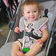 Omara is registered to the contest to win money with this photo: baby, child, clothing, cute, face, feet, footwear, happy, harness, indoor, infant, keys, mickey_mouse, person, pink, seatbelt, sitting, smile, stroller, toy