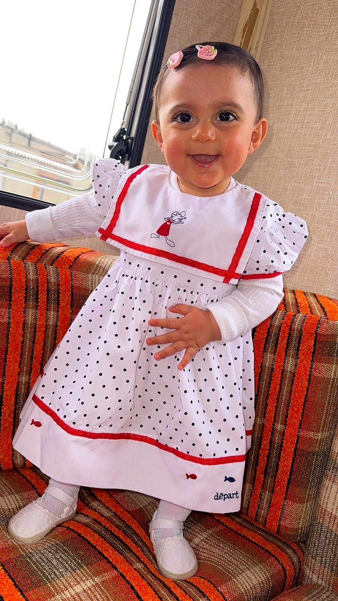 Ysalia participe au concours pour gagner de l'argent avec cette photo : toddler, child, smiling, dress, polka_dot, hair_clip, indoor, couch, orange, patterned, white_shoes, window, happy, cute, socks, long_sleeve, fabric, person, portrait, baby