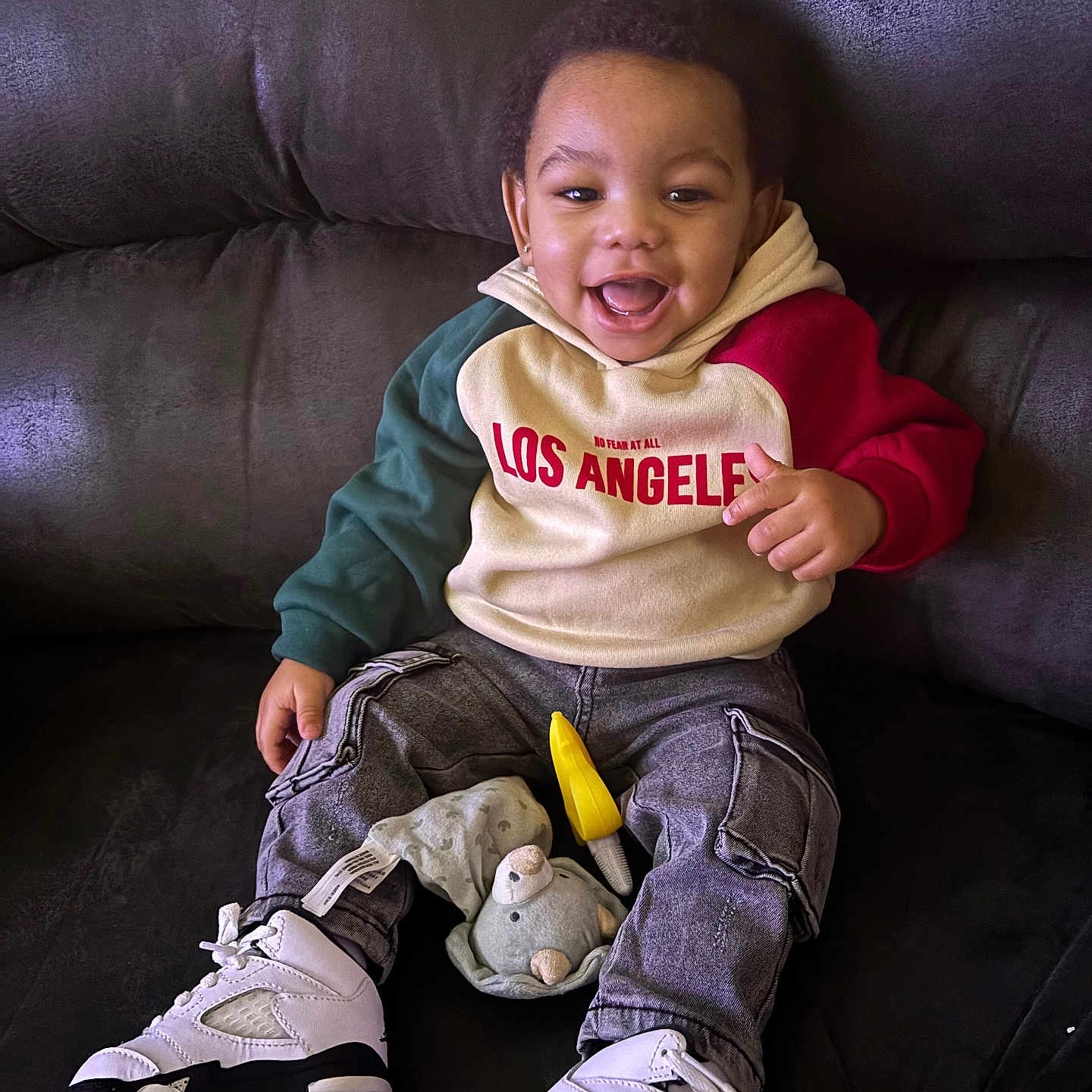 Baby John is registered to the contest to win money with this photo: bodypart, boy, child, clothing, couch, face, finger, footwear, furniture, hand, happy, head, male, pants, person, photography, portrait, shoe, sitting, sneaker