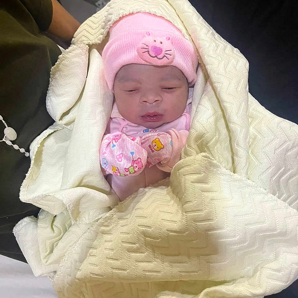 Eliana is registered to the contest to win money with this photo: newborn, baby, infant, sleeping, pink_hat, kitty_hat, mittens, blanket, swaddled, portrait, face, indoors, cozy, clothing, textile, cream_blanket, seated, car_seat, cuddled, photography