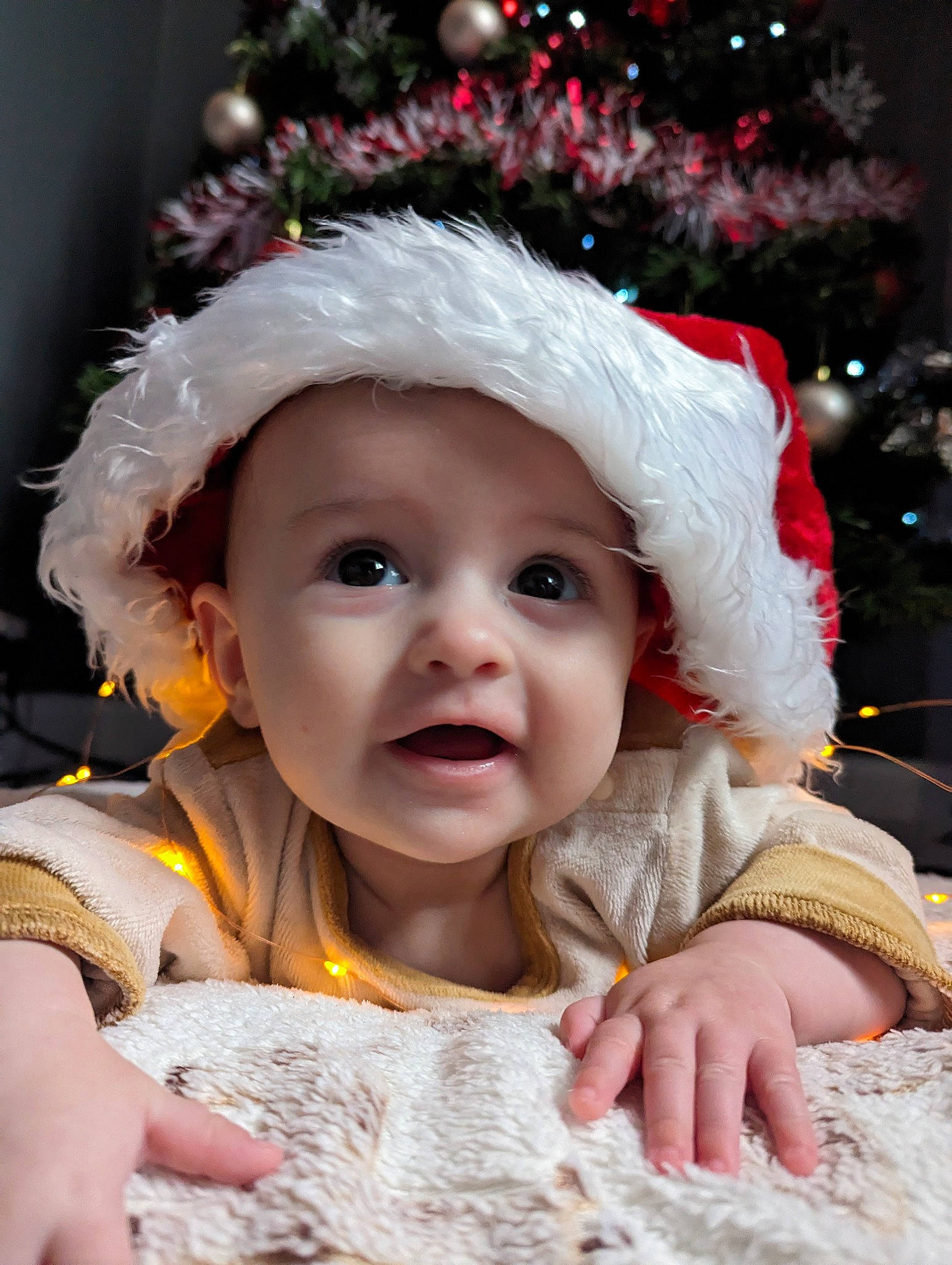 Inês is registered to the contest to win money with this photo: baby, baby_toddler_clothing, beauty, child, christmas, christmas_decoration, christmas_eve, christmas_tree, costume_hat, event, facial_expression, fun, fur, happy, headgear, headwear, holiday, person, santa_claus, skin