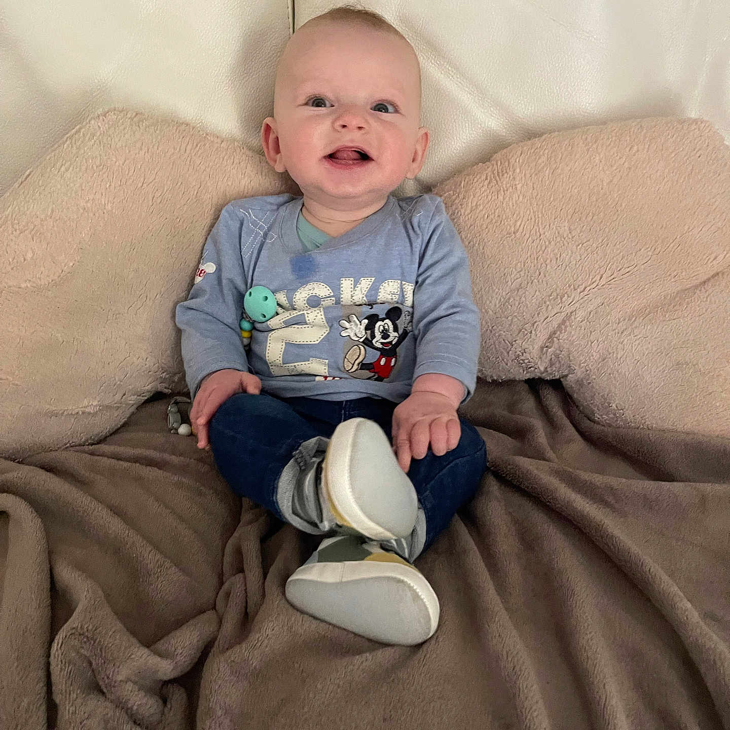 Elie participe au concours pour gagner de l'argent avec cette photo : baby, blanket, blue_clothing, child, comfort, couch, cozy, face, footwear, happy, head, home, indoor, jeans, mickey_mouse, person, shirt, shoes, sitting, smiling