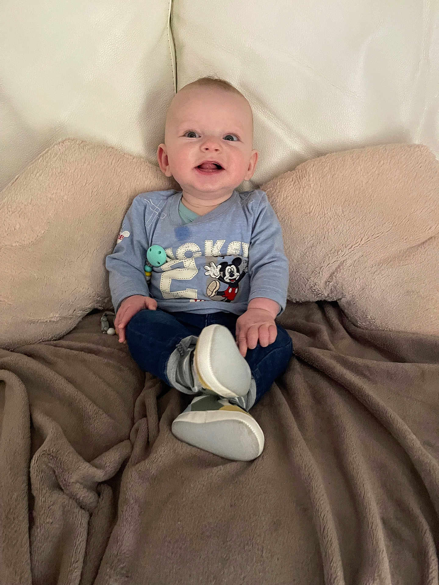 Elie participe au concours pour gagner de l'argent avec cette photo : baby, smiling, mickey_mouse, shirt, blue_clothing, jeans, shoes, blanket, couch, indoor, happy, child, person, sitting, face, head, footwear, cozy, comfort, home