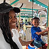amusement_park, blue_shirt, braids, cap, carousel, child, childhood, entertainment, family, fun, happy, horse, lights, outdoor, people, portrait, ride, smile, white_shirt, woman
