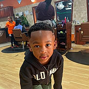 Nasir is registered to the contest to win money with this photo: barbershop, boy, casual, child, clothing, face, floor, furniture, haircut, hairstylist, hoodie, indoor, light, mirror, people, person, portrait, smile, standing, wooden_floor