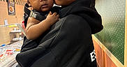 Amir is registered to the contest to win money with this photo: baby, child, young_adult, person, indoor, holding, face, expression, black_hoodie, curly_hair, restaurant, counter, food, tile_floor, light_fixture, wall, portrait, looking_at_camera, hand, casual_clothing
