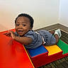 baby, carpet, child, clothing, colorful, corner, face, floor, happy, head, indoor, padded_ramp, person, play, playground_equipment, shorts, smiling, socks, toddler, wall