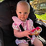 baby, child, stroller, toy, pink_clothing, seatbelt, mesh_screen, outdoor, sunlight, infant, cute, holding, seat, portrait, summer, nature, grass, face, person, happy