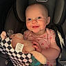 baby, child, car_seat, plush_toy, fabric_book, smiling, happy, infant, pink_clothing, heart_pattern, seatbelt, cute, indoor, portrait, person, childhood, toy, young, sitting, bright