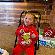 Mariah is registered to the contest to win money with this photo: child, toddler, girl, smiling, red_hair, hair_bows, grinch, christmas, sweatshirt, red_clothing, candy_cane, sitting, chair, indoor, wood_paneling, carpet, television, beverages, water_bottles, portrait