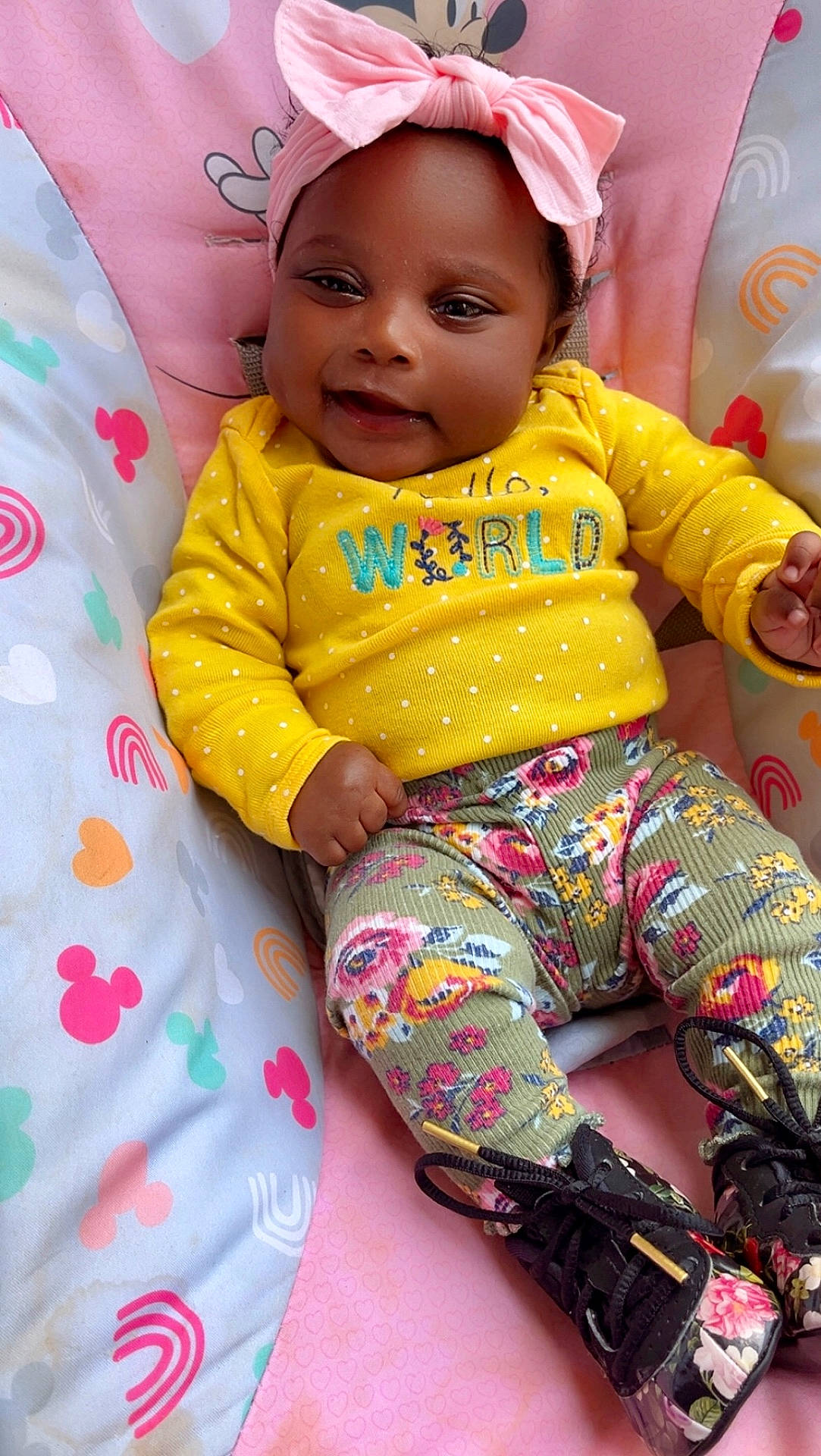 baby, baby_fashion, child, clothing, colorful, cushion, cute, floral_boots, floral_pants, happy, headband, indoors, mickey_mouse_pattern, patterned_cushion, pink_bow, portrait, rainbow_pattern, seated, smiling, yellow_sweater