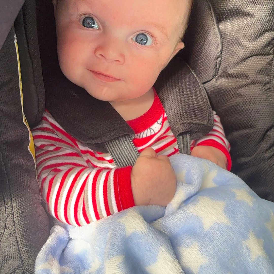 Theo is registered to the contest to win money with this photo: baby, bed, blanket, clothing, coat, cushion, face, furniture, happy, head, homedecor, jacket, newborn, pants, person, photography, portrait, sitting, smile, t_shirt