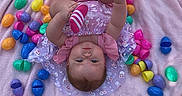 Ava joined the competition — help win amazing prizes! baby, child, pink_blanket, colorful_eggs, easter_eggs, outdoor, grass, playful, striped_socks, infant, cute, smiling, lying_down, holding_foot, clothing, person, portrait, spring, holiday, festive