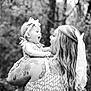 Loretta is registered to the contest to win money with this photo: baby, woman, child, tattoo, bow, hair, dress, smile, outdoor, nature, forest, black_and_white, happy, holding, laughter, portrait, person, headband, long_hair, arm