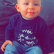 Tyméo participe au concours pour gagner de l'argent avec cette photo : baby, child, couch, cozy, cute, expression, face, furniture, hair, hand, indoors, infant, jeans, portrait, shirt, sitting, smile, striped_socks, text_on_clothing, young_child