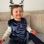 Elya participe au concours pour gagner de l'argent avec cette photo : toddler, child, smiling, indoor, reindeer_headband, blue_dress, velvet, bow, leggings, couch, cozy, plush, happy, cute, festive, portrait, sitting, baby, person, home