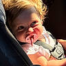 baby, infant, child, car_seat, pacifier, portrait, face, eyes, blonde_hair, smiling, sunlight, outdoor, vehicle, safety_harness, pink_clothing, seated, close_up, road_trip, greenery, photography