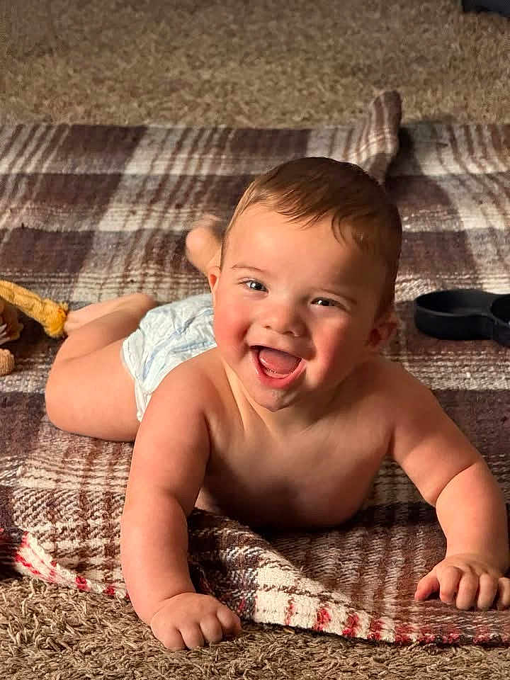 Liam joined the competition — help win amazing prizes! baby, smiling, happy, infant, blanket, plaid, carpet, diaper, child, skin, face, hand, floor, indoors, cute, one_person, young_child, portrait, lying_down, expression