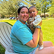 Liam is registered to the contest to win money with this photo: adult, baby, child, smile, outdoor, daylight, grass, tree, chair, person, holding, casual_clothing, shorts, tshirt, happy, greenery, park, nature, family, portrait