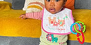 Lhayanna participe au concours pour gagner de l'argent avec cette photo : baby, child, pigtails, bib, toy, couch, cushion, living_room, carpet, clothing, sitting, curious, indoors, person, home, furniture, colorful, plastic, rings, smiling