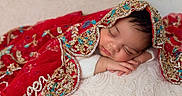 Noor is registered to the contest to win money with this photo: baby, child, close_up, cozy, cute, decorative_fabric, face, gold_embroidery, hand, indoors, infant, newborn, peaceful, portrait, red_shawl, relaxed, resting, sleeping, soft_cushion, warm