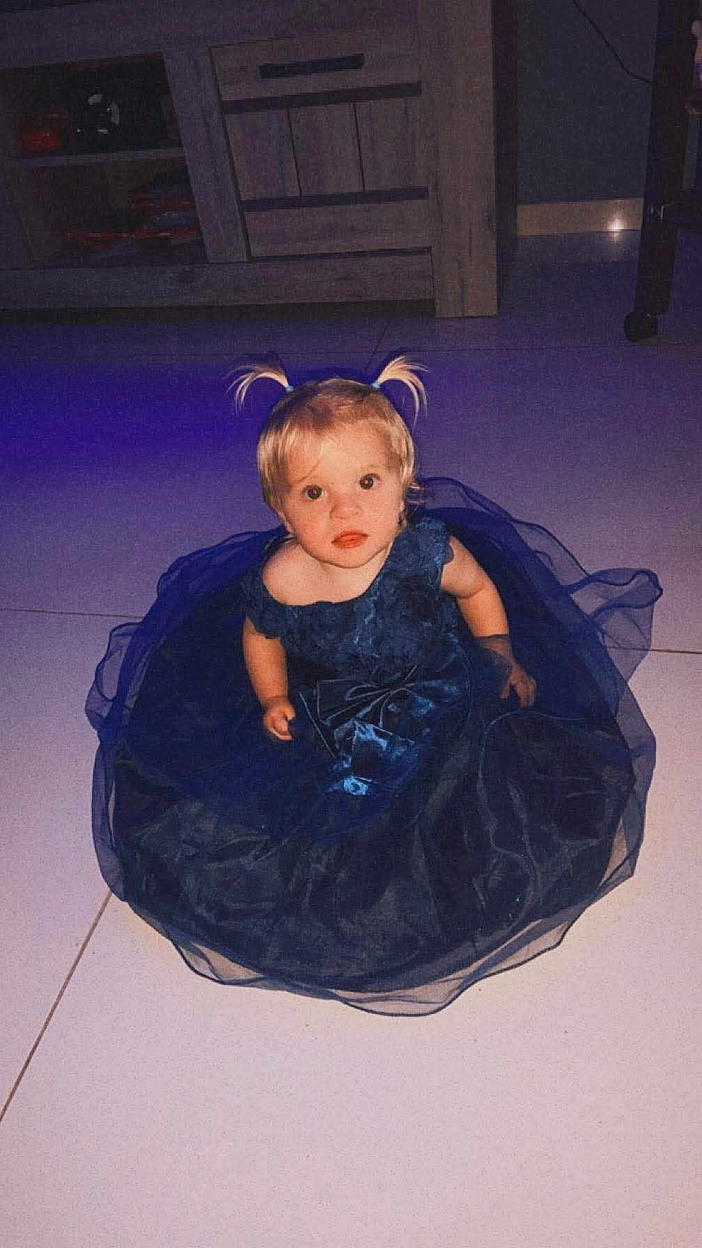 Ruby a rejoint le concours — aidez-le/la à gagner de superbes lots ! toddler, child, indoor, dress, blue_dress, pigtails, blonde_hair, floor, tile_floor, cabinet, furniture, curious, sitting, portrait, person, baby, cute, young_child, looking_up, soft_lighting