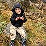 adventure, boy, casual, casual_clothing, child, daylight, dinosaur_boots, dirt, fun, grass, happy, hoodie, nature, outdoor, playful, rain_boots, rock, sitting, smiling, young_child