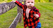 Waylon Kash joined the competition — help win amazing prizes! baby, child, toddler, outdoor, portrait, standing, grass, field, fence, wood, wooden_fence, plaid_shirt, red_clothing, blue_pants, blond_hair, face, focused, rural, nature, photography