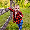 baby, child, toddler, outdoor, portrait, standing, grass, field, fence, wood, wooden_fence, plaid_shirt, red_clothing, blue_pants, blond_hair, face, focused, rural, nature, photography