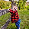 child, baby, toddler, portrait, smiling, outdoor, nature, grass, tree, branches, wood, plaid_shirt, red_clothing, blue_jeans, barefoot, standing, playful, countryside, greenery, daylight