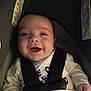 baby, infant, smiling, car_seat, carseat_strap, buckle, seat, baby_clothes, onesie, closeup, portrait, happy, laughing, indoor, blurry, soft_lighting, hand, head, face, child