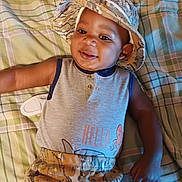 Ja'Juan is registered to the contest to win money with this photo: baby, child, smiling, hat, camouflage, plaid, blanket, sleeveless_shirt, octopus_graphic, casual_clothing, infant, lying_down, indoors, cute, happy, portrait, person, apparel, headwear, patterned_clothing