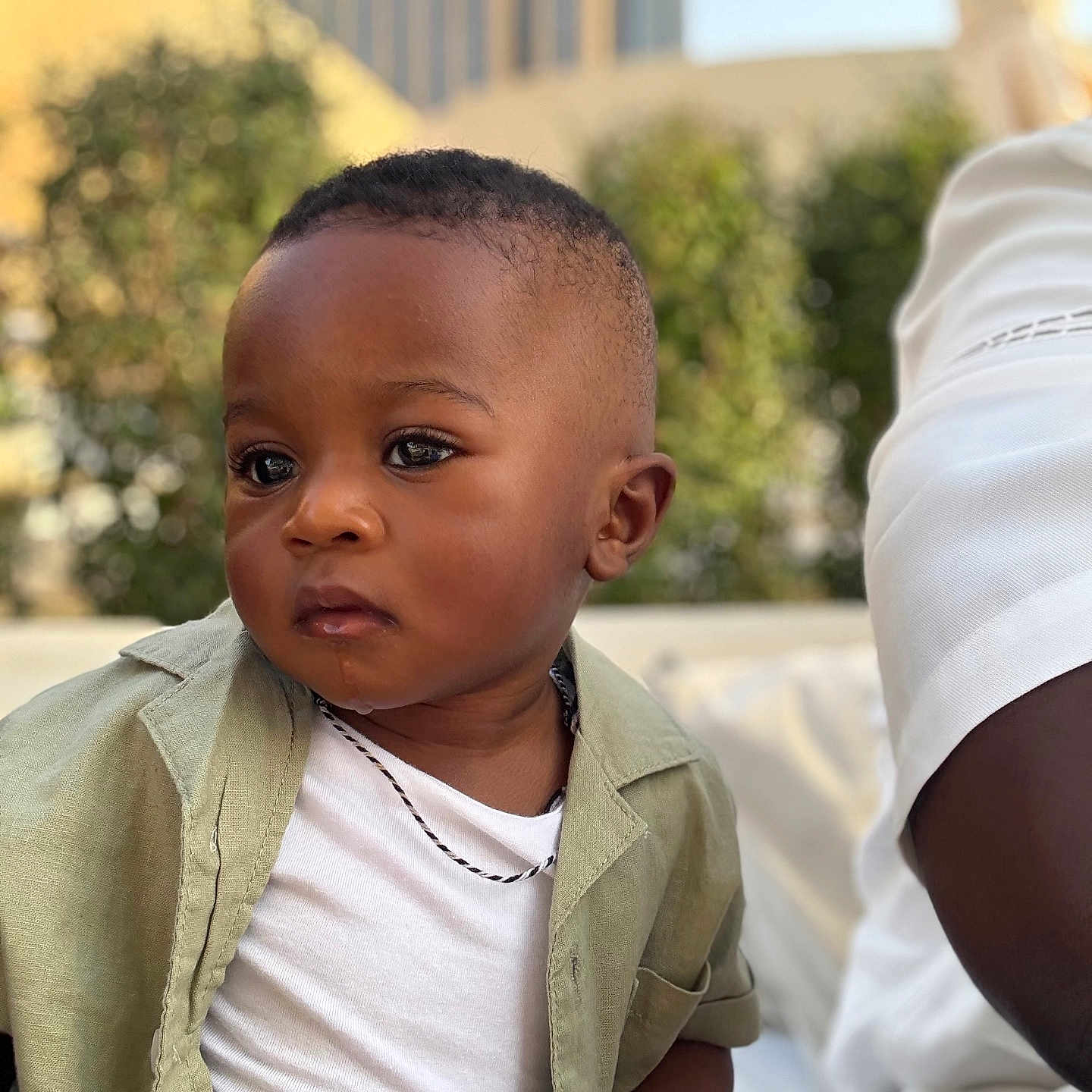Ahmed a rejoint le concours — aidez-le/la à gagner de superbes lots ! blurred_background, boy, casual_clothing, child, daylight, expression, face, green_jacket, hand, necklace, outdoor, person, portrait, short_hair, sitting, skin, toddler, urban, white_shirt, young_child