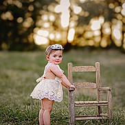 Dakota joined the competition — help win amazing prizes! baby, barefoot, child, cute, field, flower_crown, grass, greenery, innocence, lace_dress, nature, outdoor, portrait, smiling, standing, summer, sunset, toddler, wooden_chair, young_child