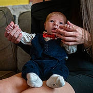 Liam participe au concours pour gagner de l'argent avec cette photo : baby, woman, infant, holding_hands, bow_tie, vest, socks, couch, indoor, brick_wall, portrait, seated, long_hair, black_dress, curious_expression, casual, human, closeup, family, togetherness