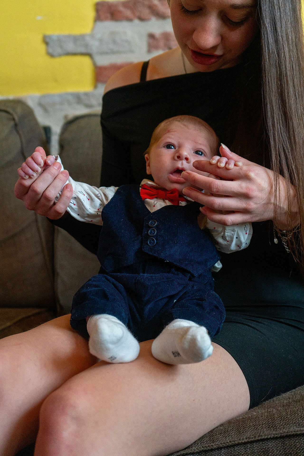 Liam participe au concours pour gagner de l'argent avec cette photo : baby, woman, infant, holding_hands, bow_tie, vest, socks, couch, indoor, brick_wall, portrait, seated, long_hair, black_dress, curious_expression, casual, human, closeup, family, togetherness