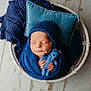 newborn, baby, sleeping, blue_knit, blanket, hat, teddy_bear, basket, pillow, wooden_floor, cozy, portrait, infant, cute, wrapped, hands, peaceful, soft_lighting, indoors, resting
