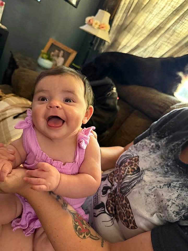 Avery is registered to the contest to win money with this photo: baby, child, smile, happy, pink_clothing, tattoo, arm, person, dog, couch, lamp, flowers, photo_frame, indoor, home, furniture, holding, cute, portrait, living_room