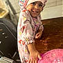 blurred_background, child, colorful, cute, face, furniture, hand, happy, home, indoors, pajamas, person, pink, playful, portrait, shower_cap, smiling, table, toy, wooden_table