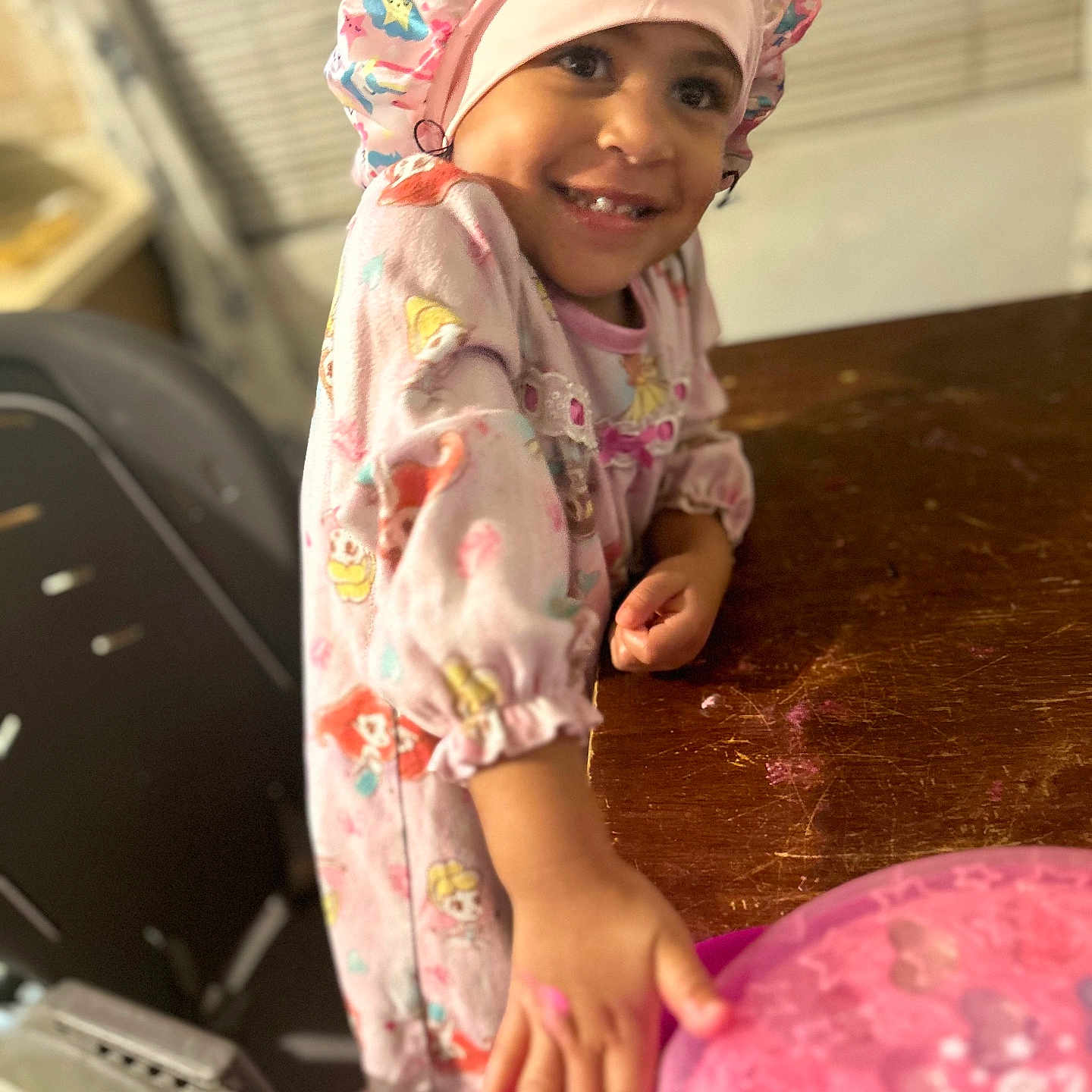 Molli is registered to the contest to win money with this photo: blurred_background, child, colorful, cute, face, furniture, hand, happy, home, indoors, pajamas, person, pink, playful, portrait, shower_cap, smiling, table, toy, wooden_table