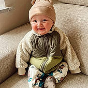 Stanley joined the competition — help win amazing prizes! baby, child, smile, hat, beanie, jacket, fleece, couch, indoor, window, cozy, warm_clothing, sitting, cute, infant, happy, portrait, sock, patterned_pants, home