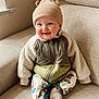 baby, child, smile, hat, beanie, jacket, fleece, couch, indoor, window, cozy, warm_clothing, sitting, cute, infant, happy, portrait, sock, patterned_pants, home