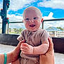 baby, smiling, hands, outdoor, blue_sky, clouds, clothing, person, infant, happy, holding, festive_decorations, pole, railing, daylight, casual_wear, cute, portrait, skin, expression